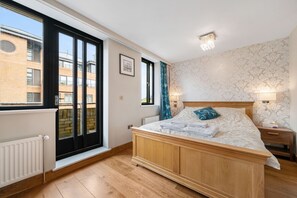 Quarto com cama grande, janela com vista para um edifício, radiador e mesa de cabeceira com luminária.