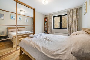 Ein Schlafzimmer mit einem großen Bett, einem Schrank mit Spiegel, einem Bücherregal und einem Fenster mit Vorhängen.