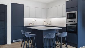Une cuisine moderne dotée d’un îlot central, de tabourets de bar, d’appareils électroménagers intégrés et d’un mur d’accent de couleur foncée.