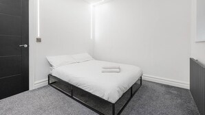 Une chambre moderne avec un lit simple, du linge de lit blanc, une porte sombre et un radiateur fixé au mur.