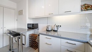 A modern kitchen with white cabinets, a granite countertop, a wine rack, and a toaster. - Spacious Kensington Apartment With City Views (London)