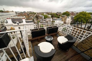 Eine Dachterrasse mit Korbmöbeln, einem Holzboden und Blick auf die Stadt.