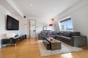 Ein modernes Wohnzimmer mit grauem Sofa, einem Couchtisch, einem flachbildfernseher an der Wand und einem großen Fenster mit Blick auf die Stadt.