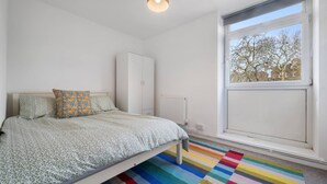 Quarto com cama, radiador, guarda-roupa e janela com vista para árvores.