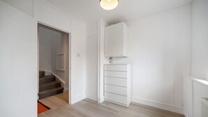 Um corredor com escada, uma porta branca e um armário embutido branco.