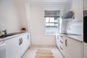 Eine kleine Küche mit weißen Schränken, einem eingebauten Backofen und einem Fenster mit Jalousien.