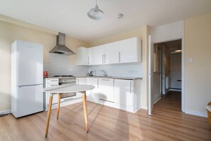 A modern kitchen with white cabinets, a white refrigerator, a gas stove, and a round table with wooden legs. - 4-bed Maisonette With Balcony (London)