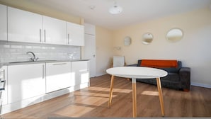 A modern kitchen with white cabinets, a white countertop, and a round table with wooden legs. - 4-bed Maisonette With Balcony (London)