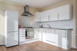 Eine moderne Küche mit weißen Schränken, einem eingebauten Backofen, einem Edelstahlkochfeld und einem Kühlschrank.