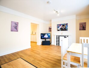 A living room with a TV, wooden flooring, white walls, and artwork. - Central Ipswich Stay for 4 Budget-friendly Convenient (Ipswich)