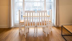 Una habitación con piso de madera, un banco blanco y ventanas grandes con cortinas.
