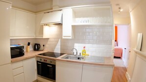 Una cocina compacta con armarios blancos, horno empotrado, microondas y un fregadero.