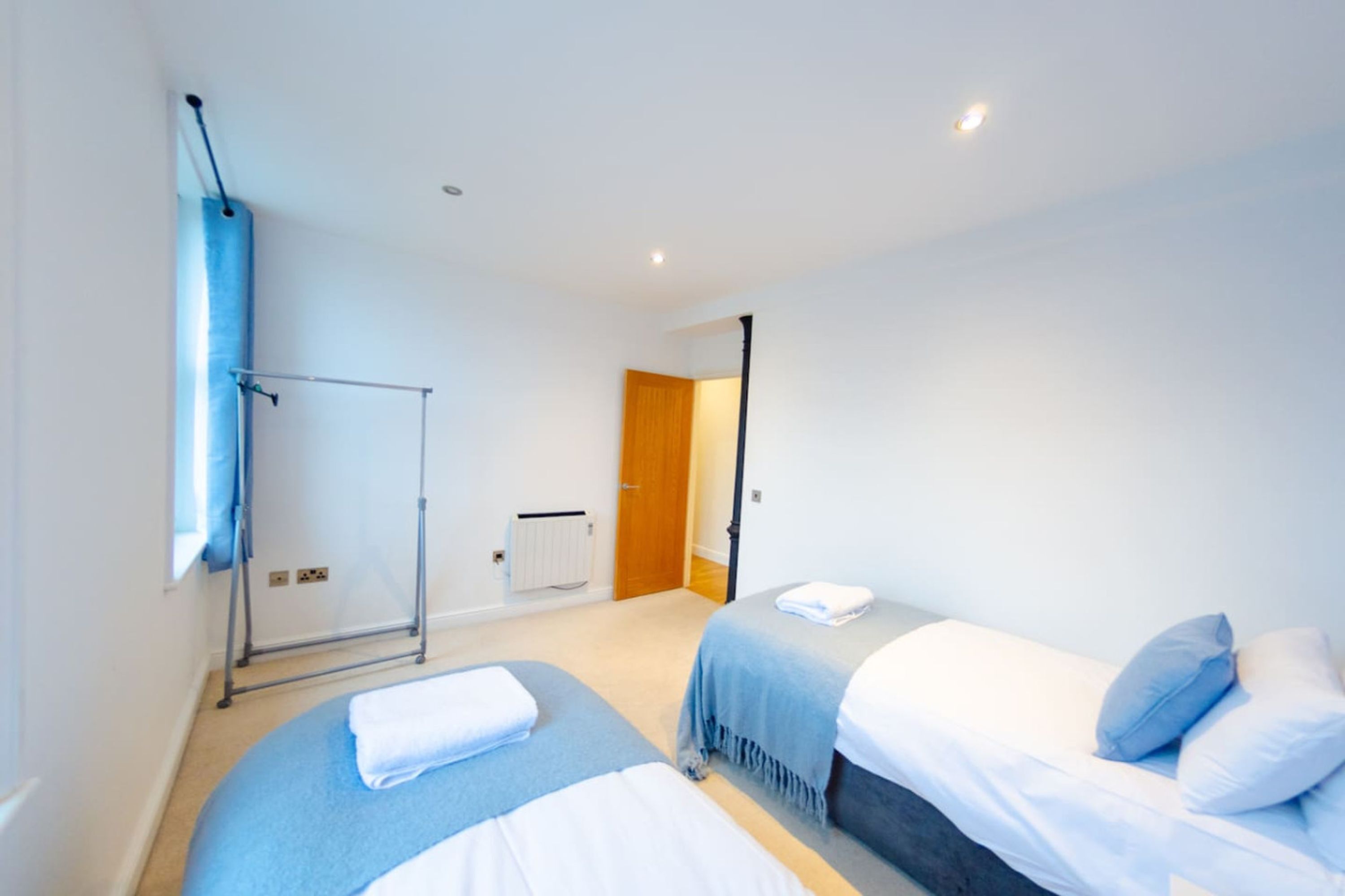 Een hotelkamer met twee bedden, een radiator, een raam met gordijnen en een deur die naar een andere kamer leidt.