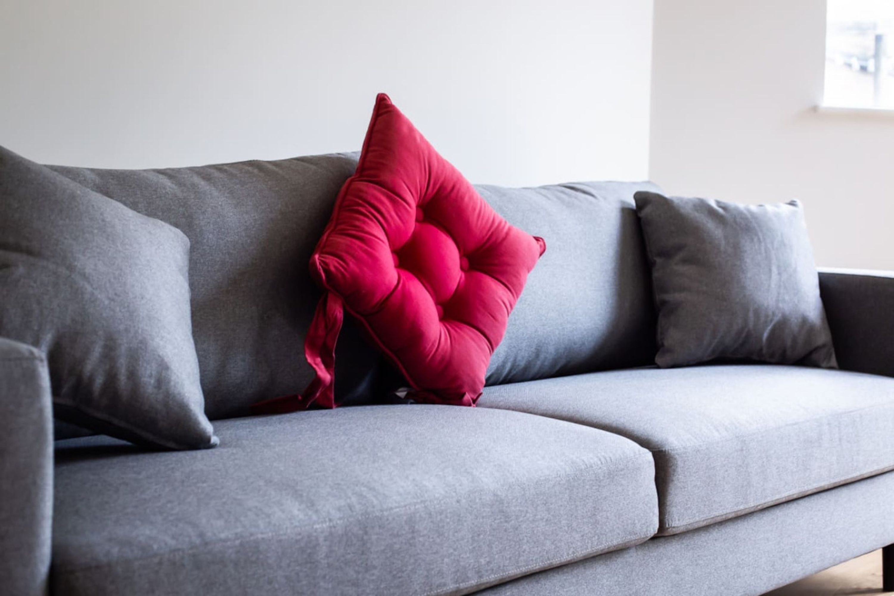 Ein graues Sofa mit einem roten Kissen und einem grauen Kopfkissen.