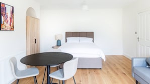 Ein Schlafzimmer mit einem Bett, einem runden Tisch, zwei Stühlen, einer Lampe und einem Bild an der Wand.