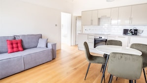 Ein modernes Wohnzimmer mit grauem Sofa, einem roten Kissen sowie einem Essbereich mit weißem Tisch und grauen Stühlen.
