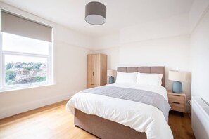 Een slaapkamer met een groot raam, een bed met hoofdeinde, een kledingkast en bedlampjes.