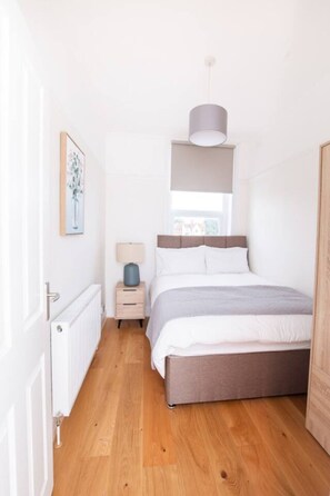 Een slaapkamer met een bed, nachtkastje, lamp en een raam met uitzicht.