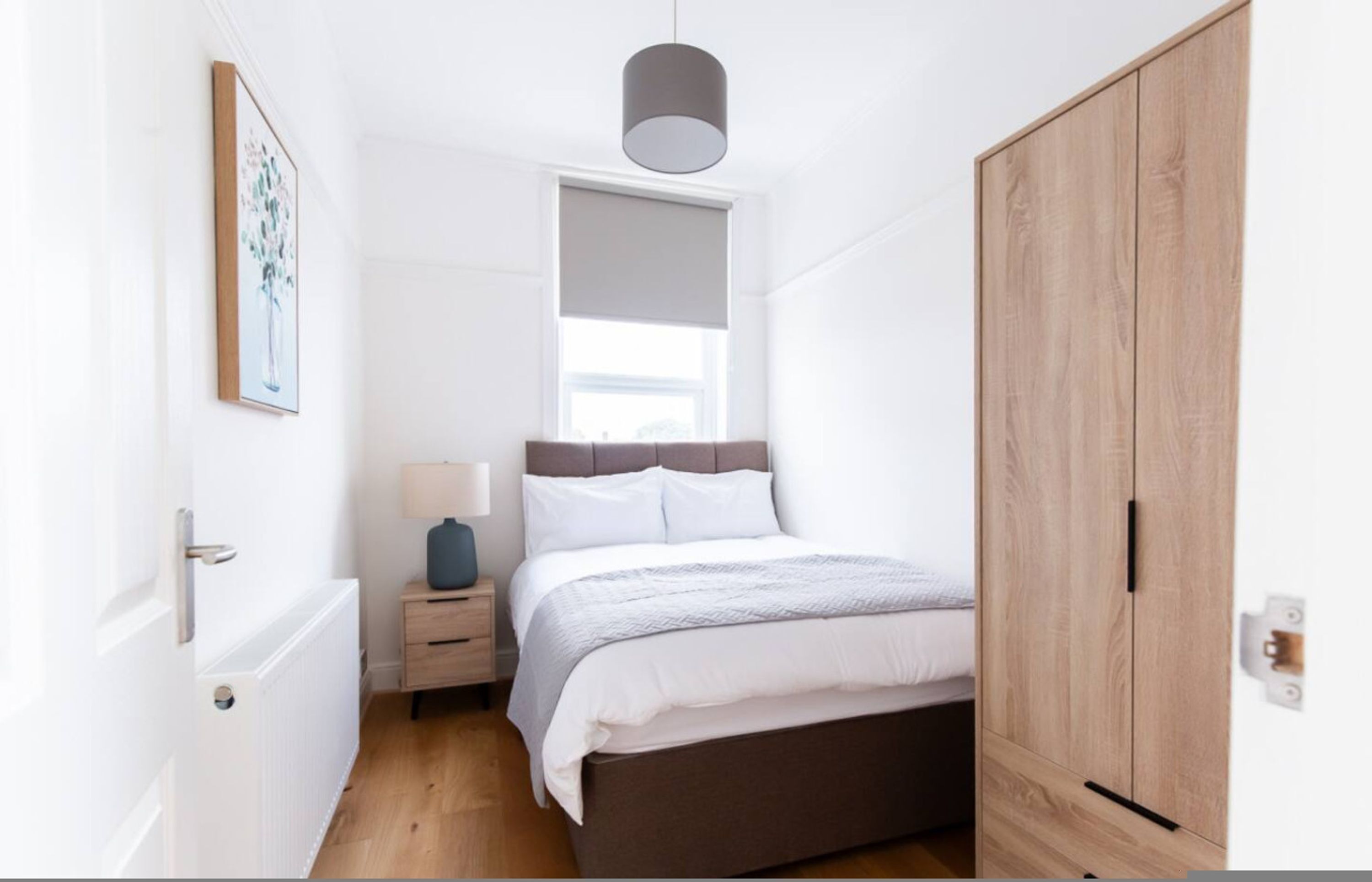 A bedroom with a bed, bedside table, lamp, window, and wardrobe.