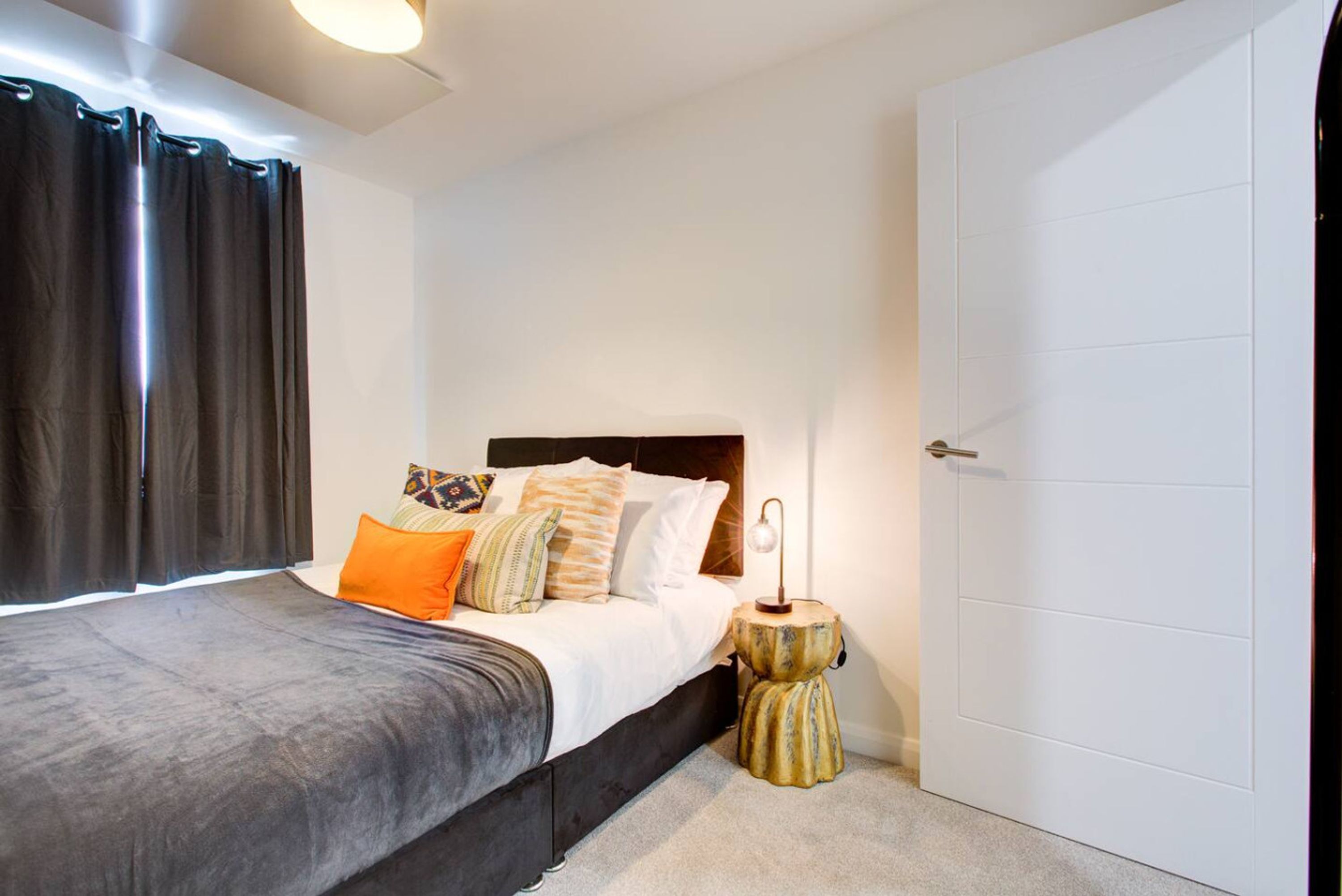 Un dormitorio con cama, almohadas, mesita de noche y una puerta.