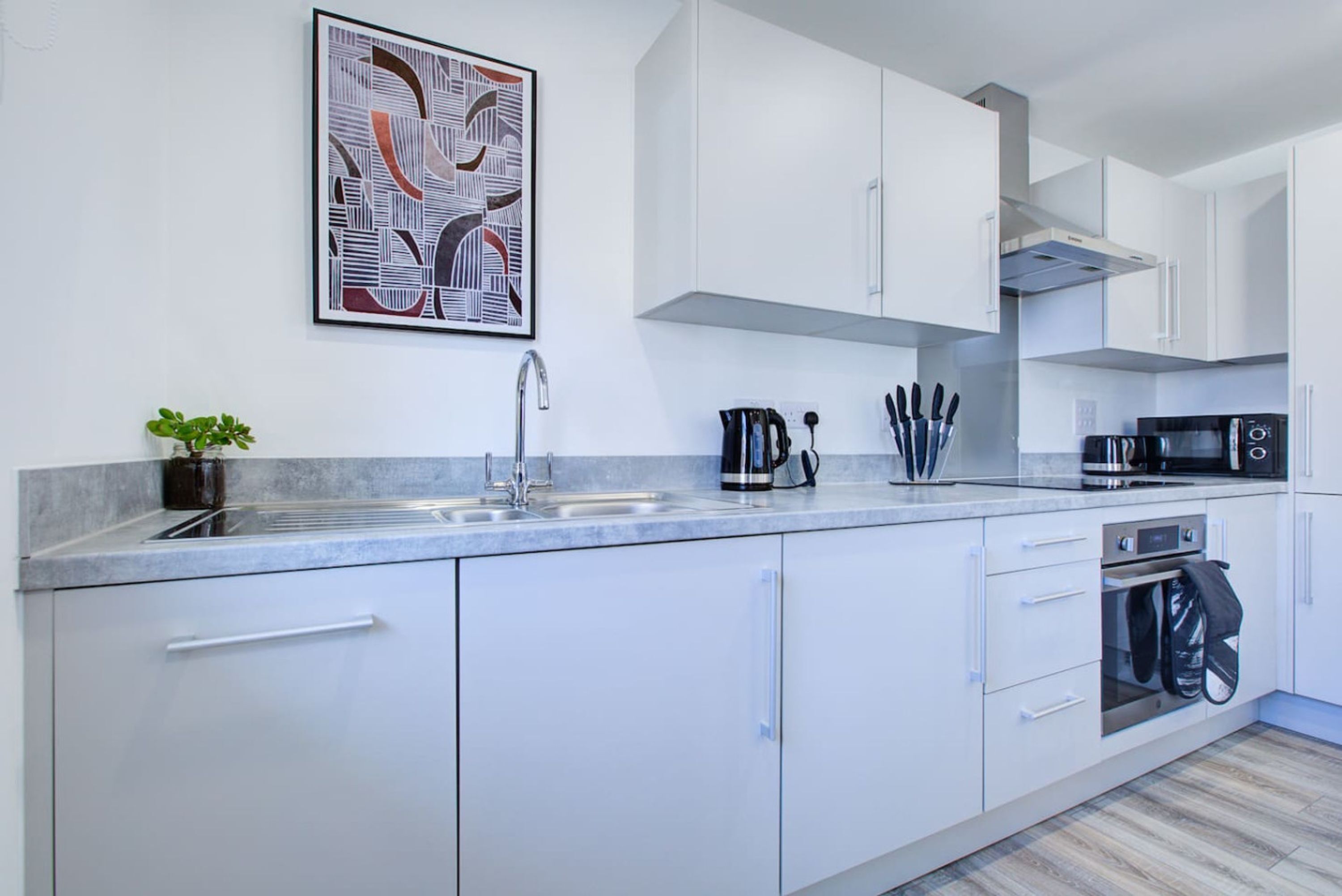 A modern kitchen with white cabinets, a stainless steel sink, a coffee maker, and a microwave.