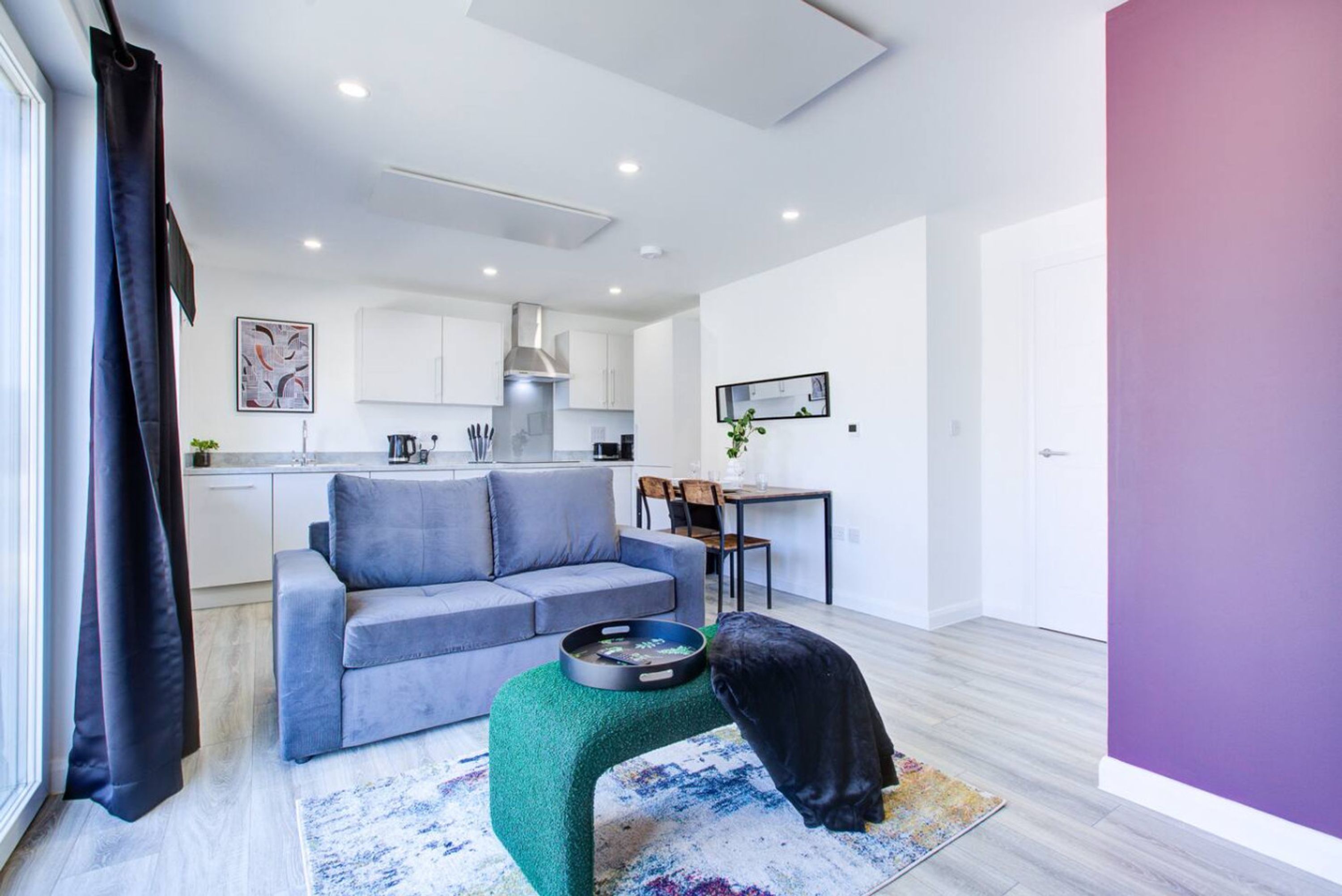 Un salon moderne avec un canapé gris, un pouf vert et un chat noir.
