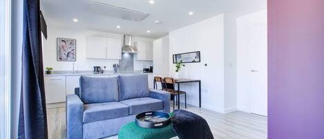 Un salon moderne avec un canapé gris, un pouf vert et un chat noir.