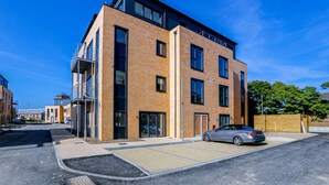A modern multi-story building with a parking area, a car, and a clear blue sky. - Penny Place Retreat Central 2bed 2bath by Station Free Parking (Ashford)