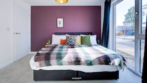 A modern bedroom with a large bed, a view of the outside, and a unique green pendant light. - Penny Place Retreat Central 2bed 2bath by Station Free Parking (Ashford)