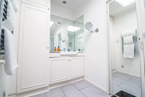 Ein modernes Badezimmer mit großem Spiegel, weißen Schränken und einer Duschkabine.