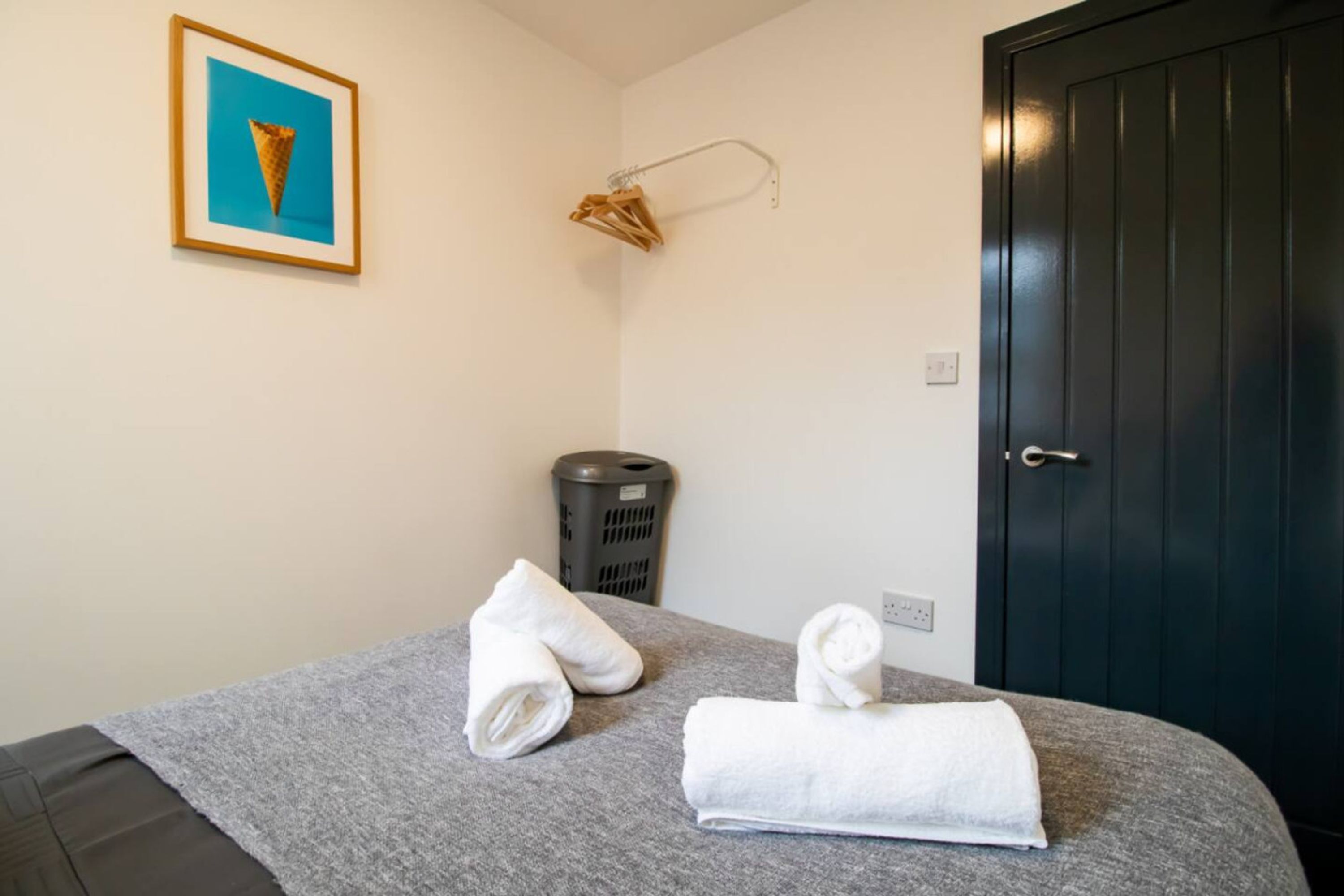 A hotel room with a bed, a framed picture on the wall, a towel rack, and a trash bin.