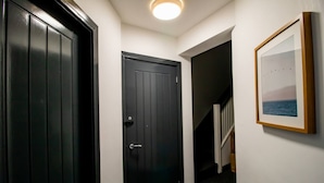 Un pasillo con una puerta negra, un cuadro en la pared y una escalera al fondo.