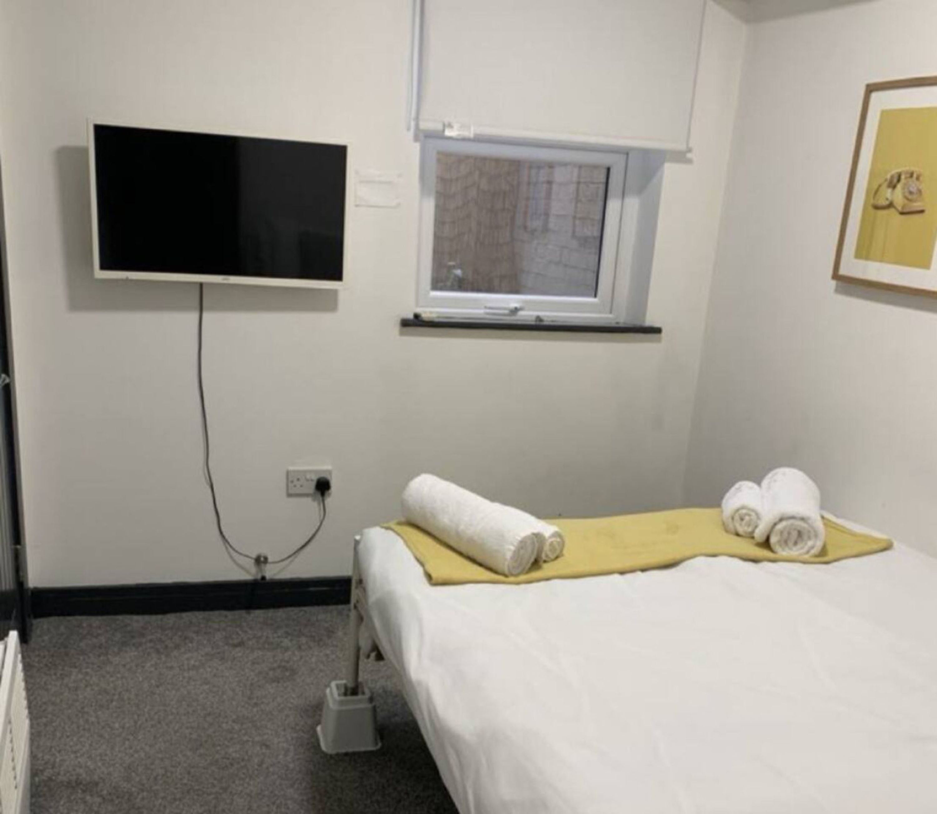 A hotel room with a bed, a television mounted on the wall, a window, and a power outlet.