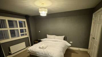 A bedroom with a bed, a radiator, a window with blinds, a chandelier, and a door.