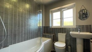 Een badkamer met bad, toilet en wastafel, met een raam en een spiegel.