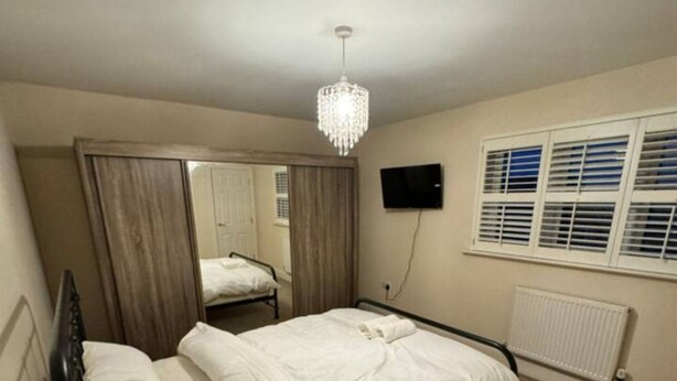 Een slaapkamer met een bed, een spiegel, een televisie en een raam met zonwering.