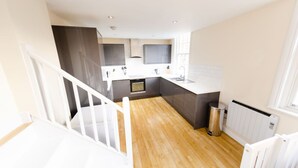 A modern kitchen with a wooden floor, white and dark grey cabinets, a stainless steel sink, and a white radiator. - Charlotte House Prime Location Urban Nest 2bed 2bath (Ipswich)