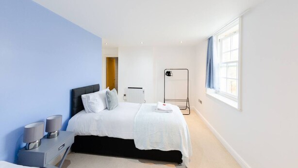 A bedroom with a bed, bedside tables, a radiator, a window with curtains, and a black radiator stand. - Charlotte House Prime Location Urban Nest 2bed 2bath (Ipswich)