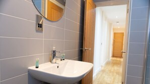 A bathroom with a white sink, a mirror, and a wooden door leading to a hallway. - Charlotte House Prime Location Urban Nest 2bed 2bath (Ipswich)