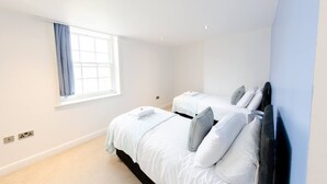 A bedroom with two beds, a window with curtains, and a light-colored carpet. - Charlotte House Prime Location Urban Nest 2bed 2bath (Ipswich)