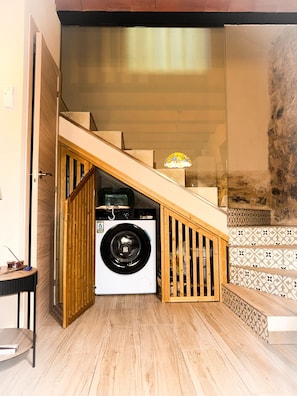 A compact living space with a washing machine, wooden staircase, and patterned tiles.