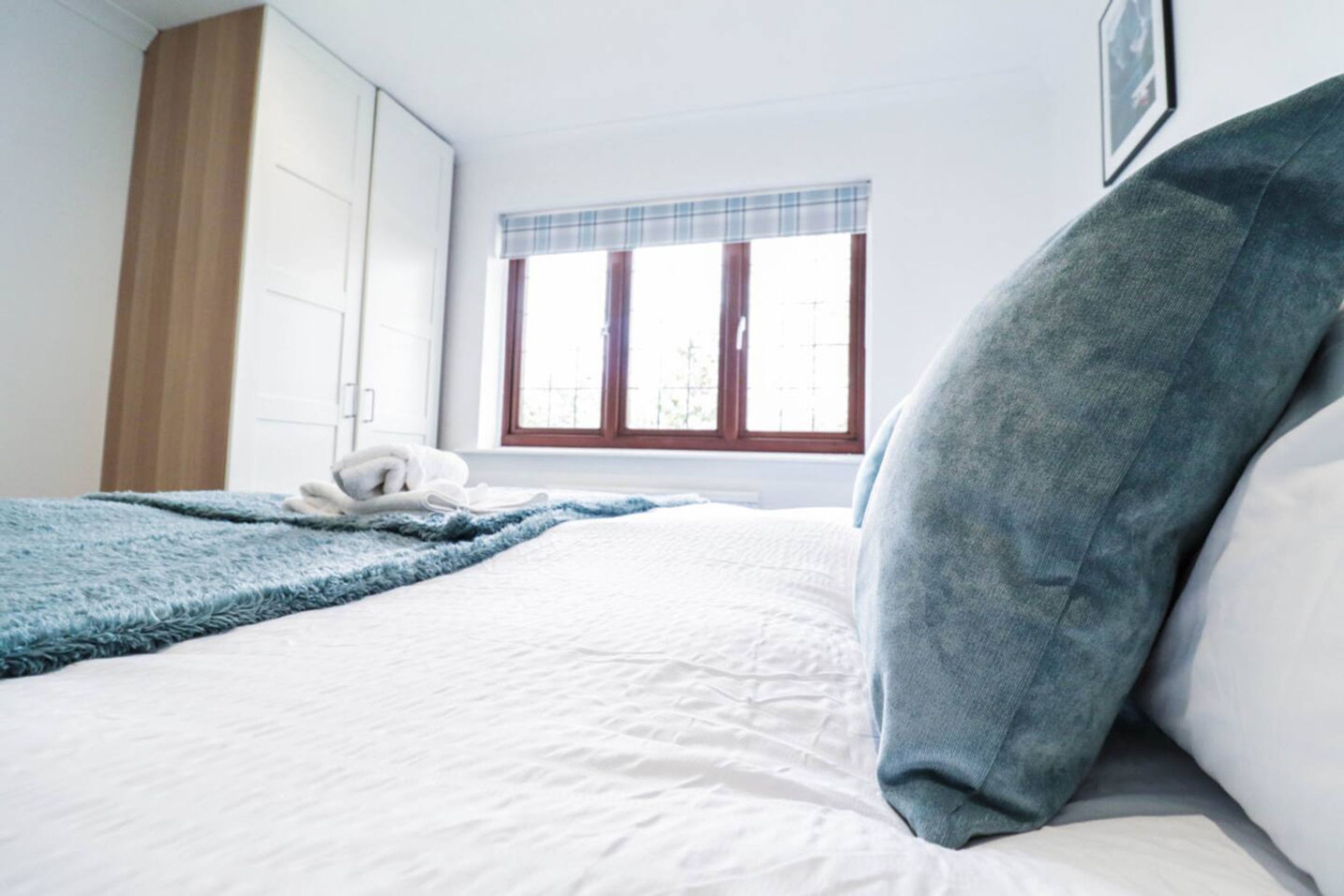 A bedroom with a bed, a window with a plaid curtain, and a wardrobe.