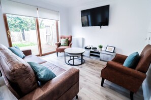 Ein modernes Wohnzimmer mit Sofa, Sesseln, Couchtisch und einem flachbildfernseher an der Wand.