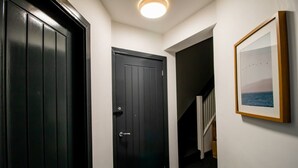 En hall med en svart dörr, en inramad tavla på väggen och en trappa i bakgrunden.