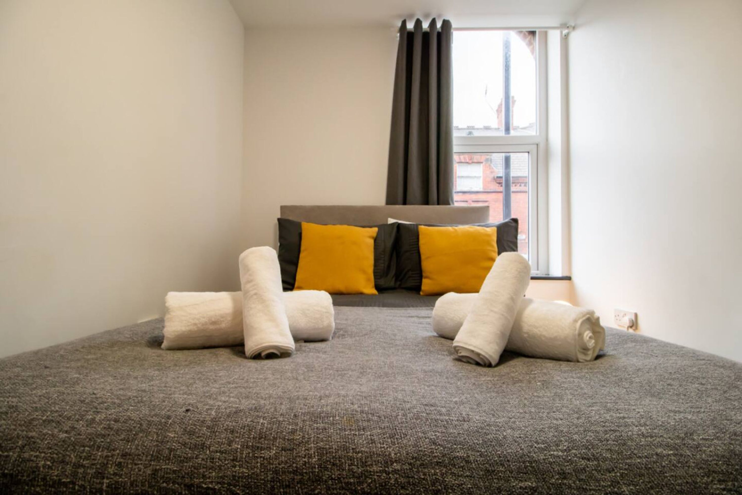 A hotel room with a bed, pillows, and rolled towels.
