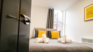 Ett hotellrum med en säng, ett fönster med gardiner, ett element och en inramad tavla på väggen.