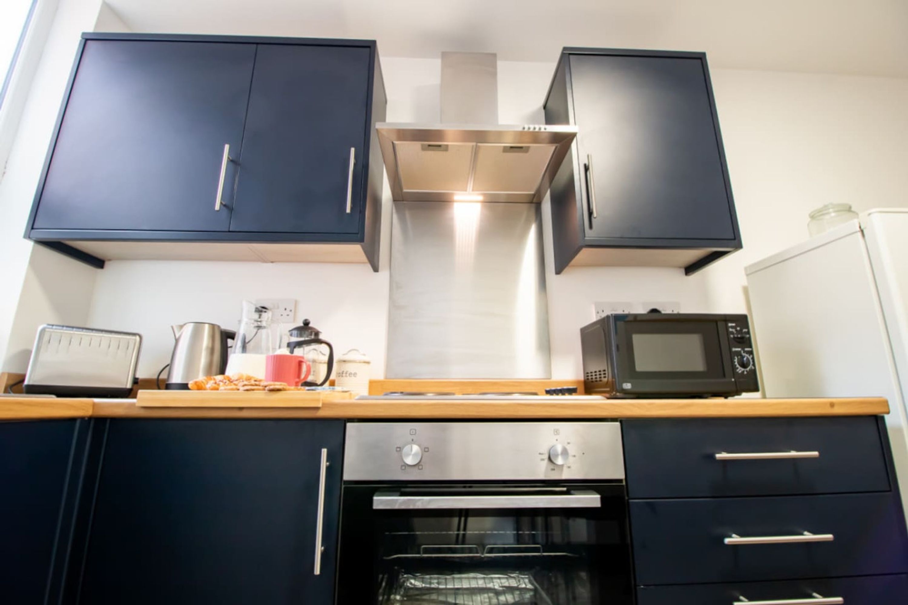 A kitchen with dark cabinets, a stainless steel range hood, a microwave, and an oven.