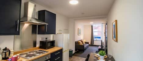 A compact kitchen with a stove, oven, microwave, and refrigerator. There is a dining area with a table and chairs, and a living room with a sofa and a TV.