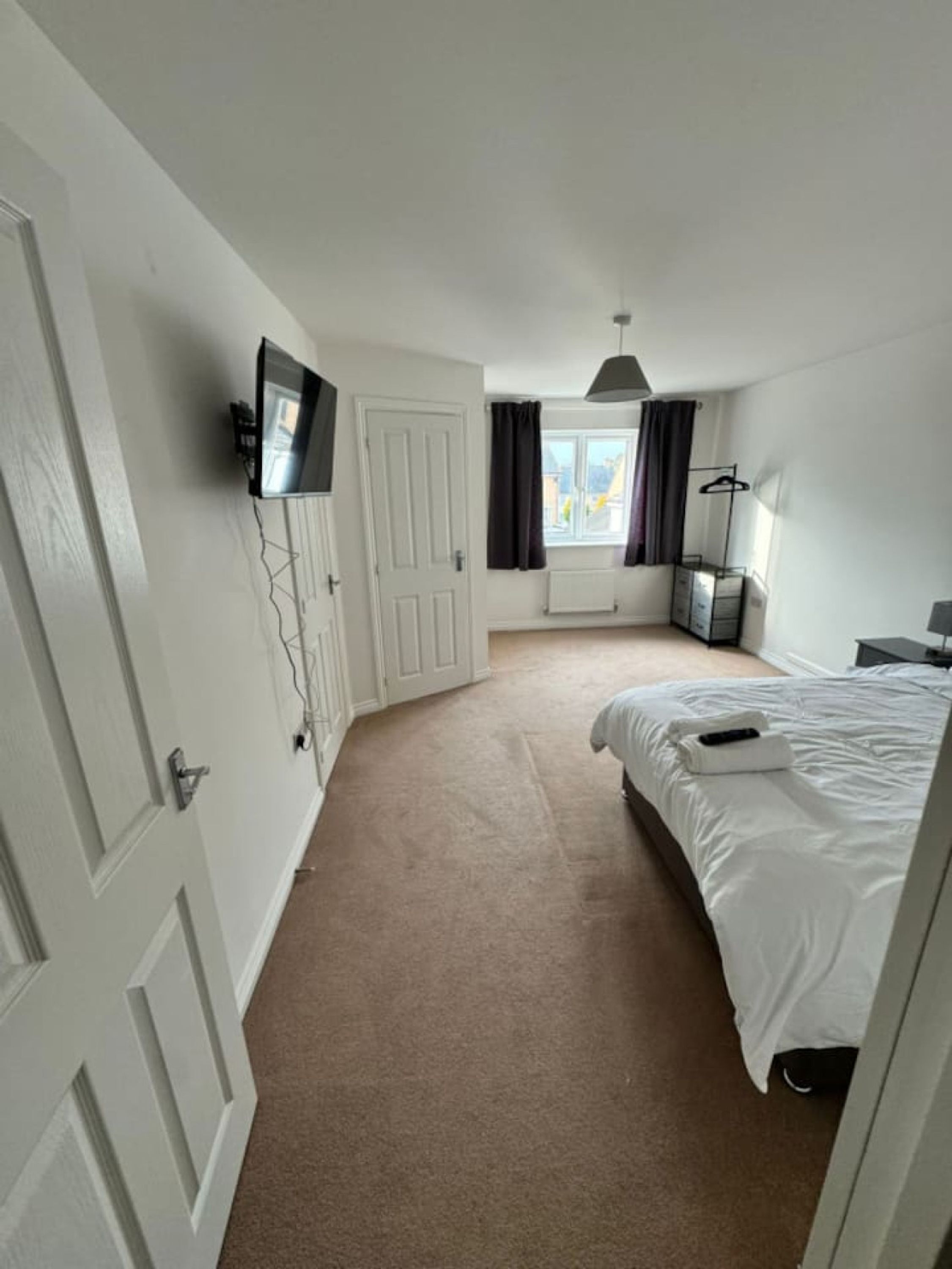 Een slaapkamer met een bed, een aan de muur bevestigde televisie, een raam met gordijnen en een radiator.