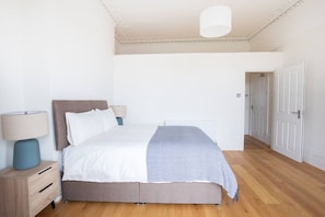 A bedroom with a bed, bedside tables, a lamp, and a door leading to another room. - Charming 2BR Sanctuary St Leonards on Sea - Flat 4 (St Leonards-On-Sea)